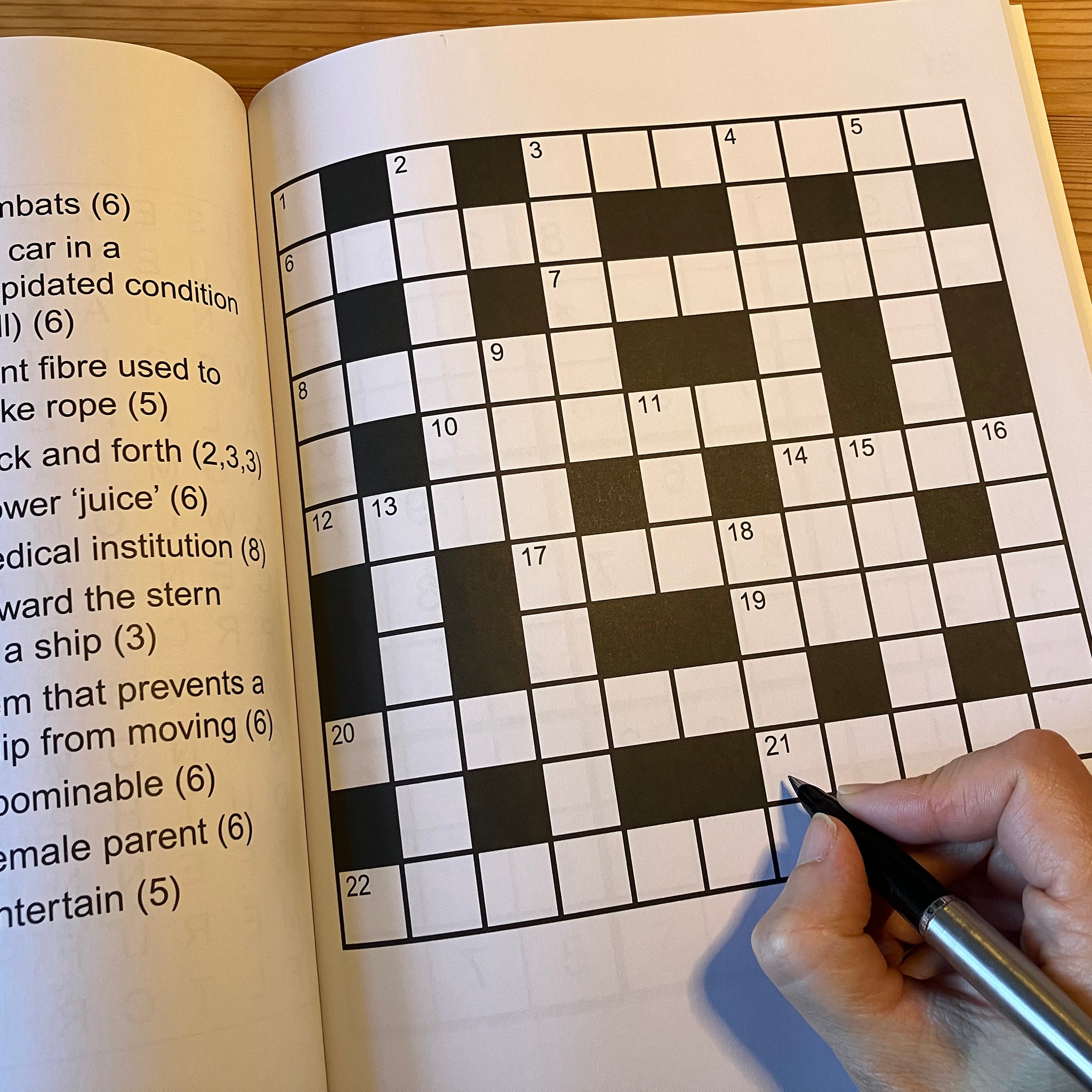 Crossword puzzle in a book with a hand holding a pen, partially filled in