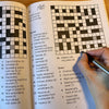 Crossword puzzle book with a hand holding a pen, partially filled in
