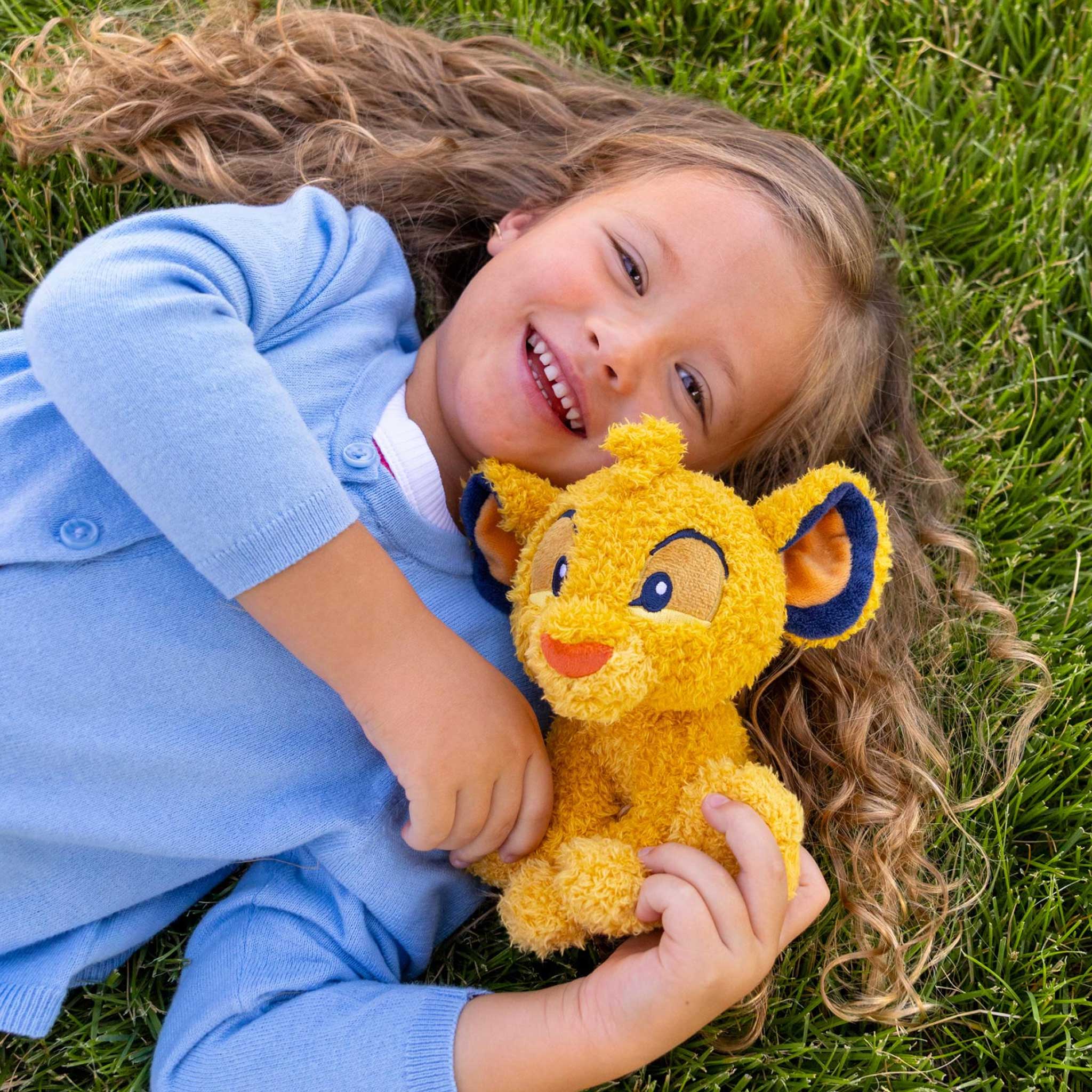 Child in blue outfit lying on grass holding a yellow plush toy