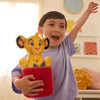 Child holding a plush toy in a red container with a room in the background