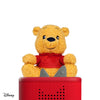 Yellow teddy bear with a red shirt on top of a red speaker with a white background