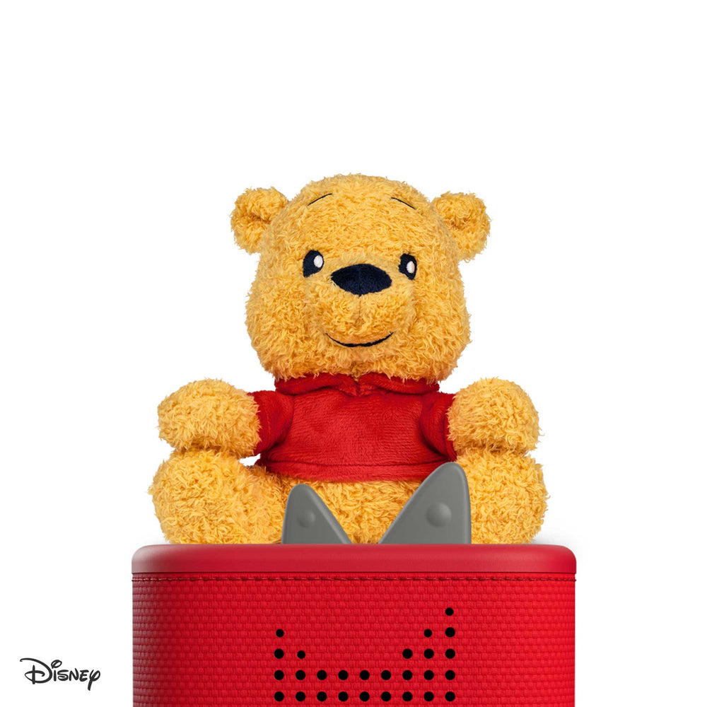 Yellow teddy bear with a red shirt on top of a red speaker with a white background