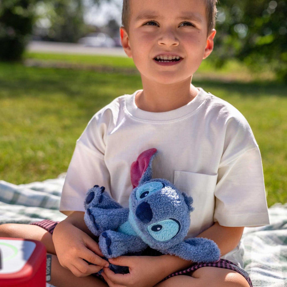 Child holding a blue teddy bear outdoors on a grassy area