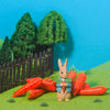 Toy rabbit with a carrot in a garden setting with trees and fence on a blue background