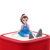 Toy figure of a girl in overalls sitting on a red toy with shark fins on a white background
