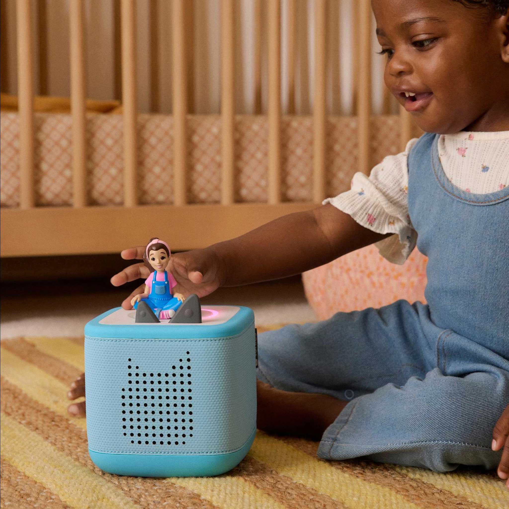Child playing with a blue toy device and figurine on a carpeted floor.