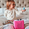 Child holding a toy figure next to a pink toy box on a bed