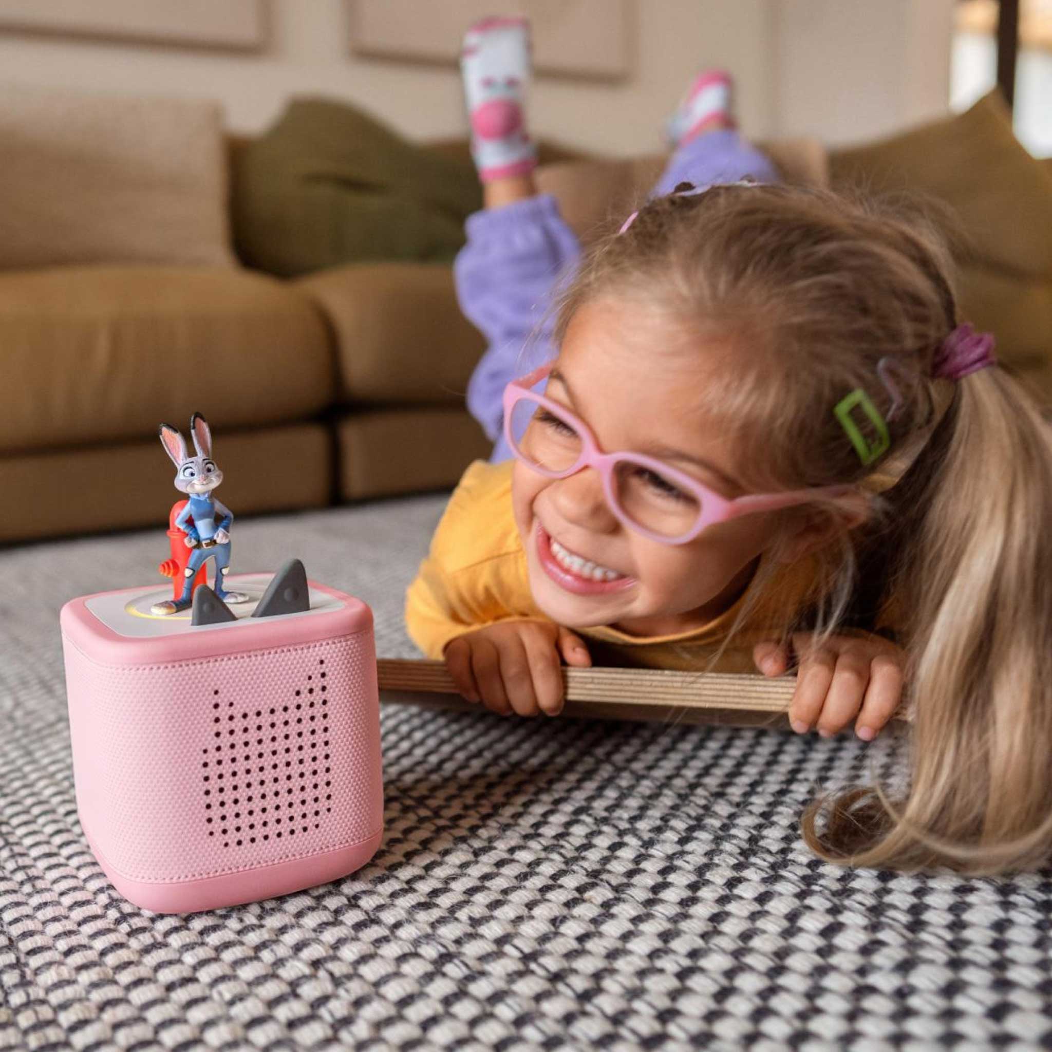 Child playing with a pink toy speaker on a patterned rug
