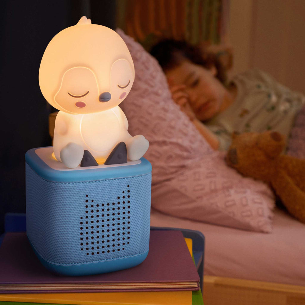 Children's night light shaped like a cartoon moon on a blue base, with a child sleeping in the background.