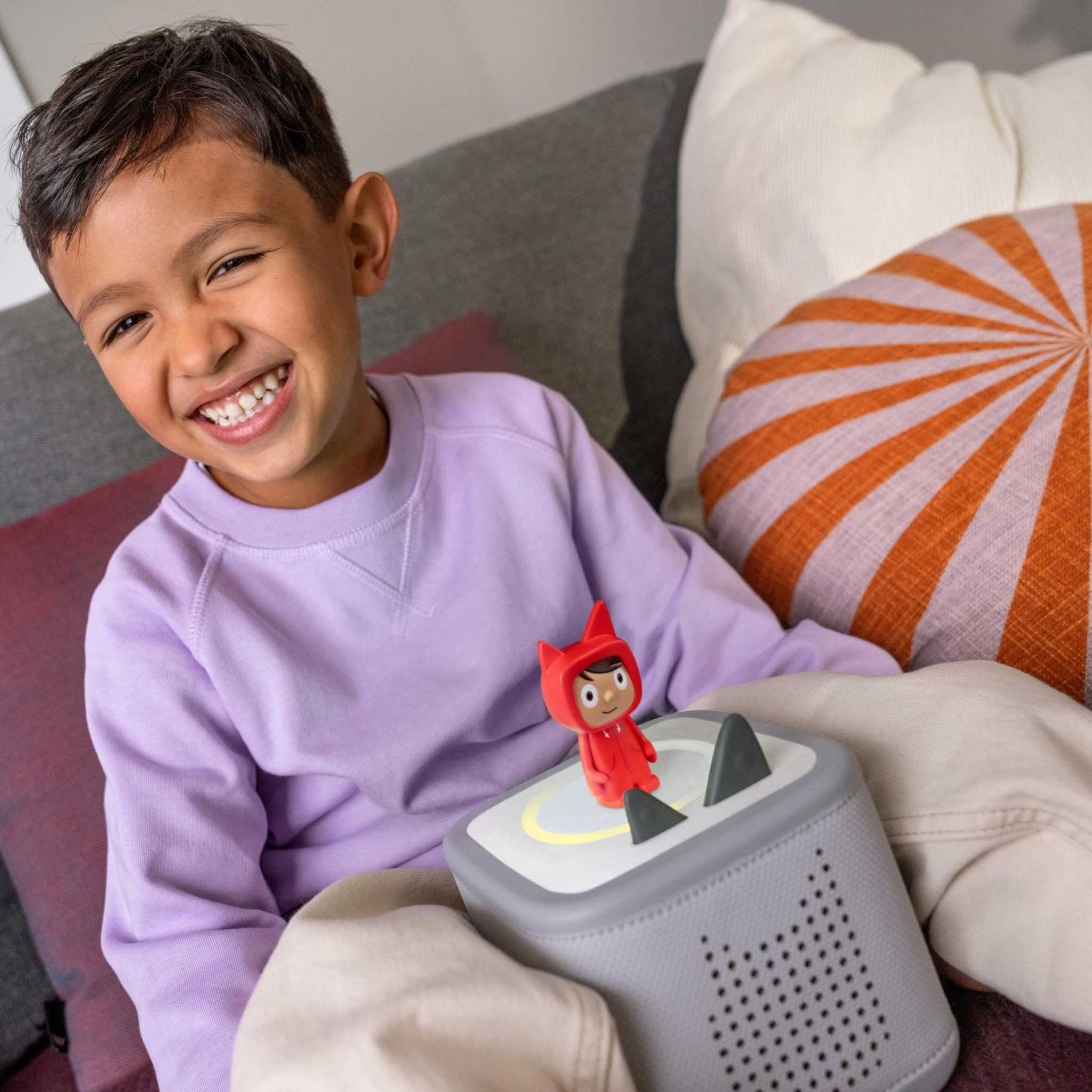Child sitting on a couch with Toniebox 2 and a small figure on top