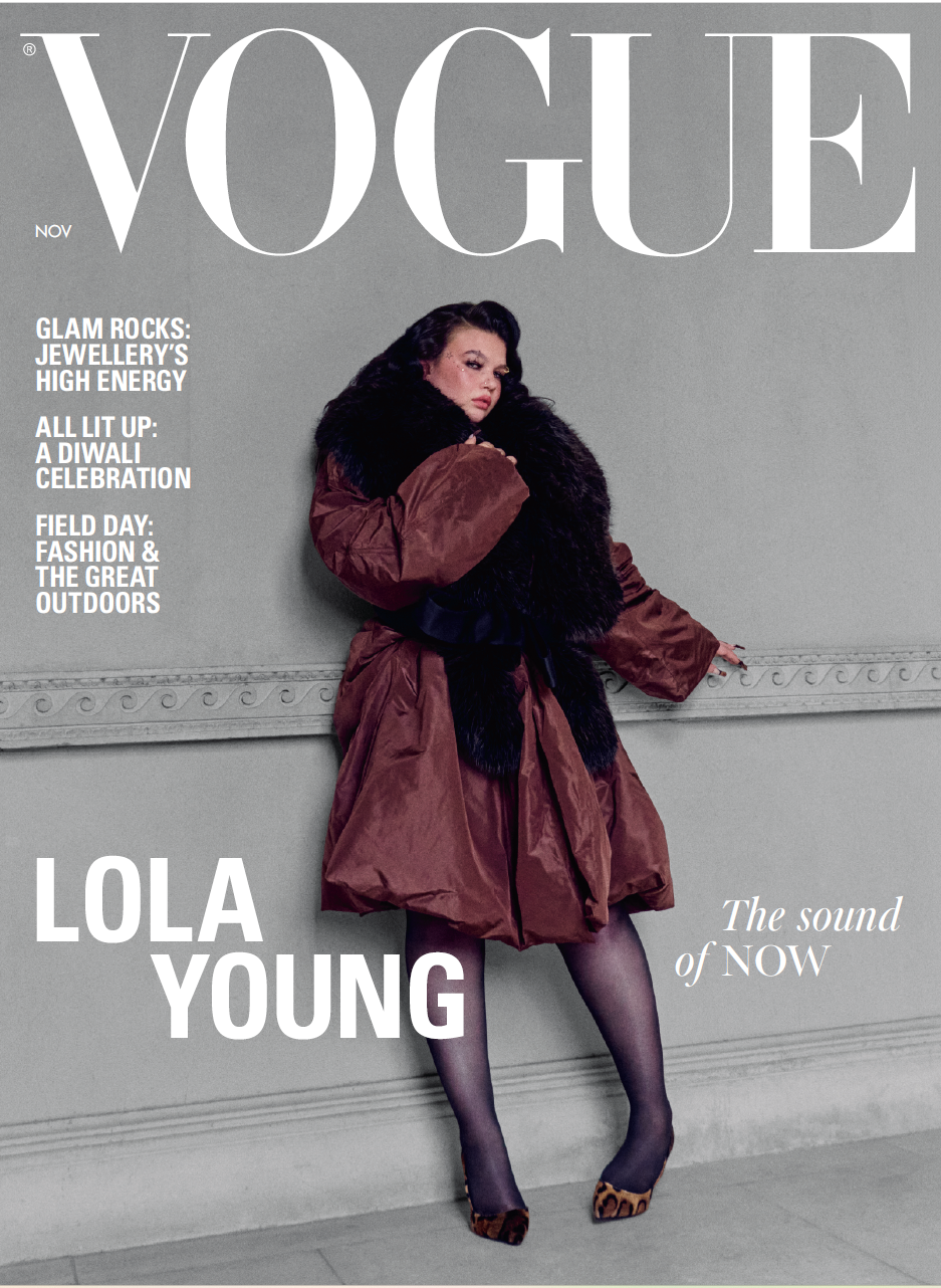 Vogue magazine cover featuring model Lola Young posing in a brown coat with a dark fur collar against a gray wall. Large white 'VOGUE' masthead and cover text are visible, with 'LOLA YOUNG' in bold at lower left.