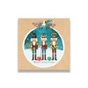 The design of the card suggests a colourful bauble in front of brown wrapping paper. Within the festive bauble, stand the three colourful Nutcracker soldiers with fancy hats, black moustaches and long white beards. Beneath their feet are the words ‘Merry Christmas’.