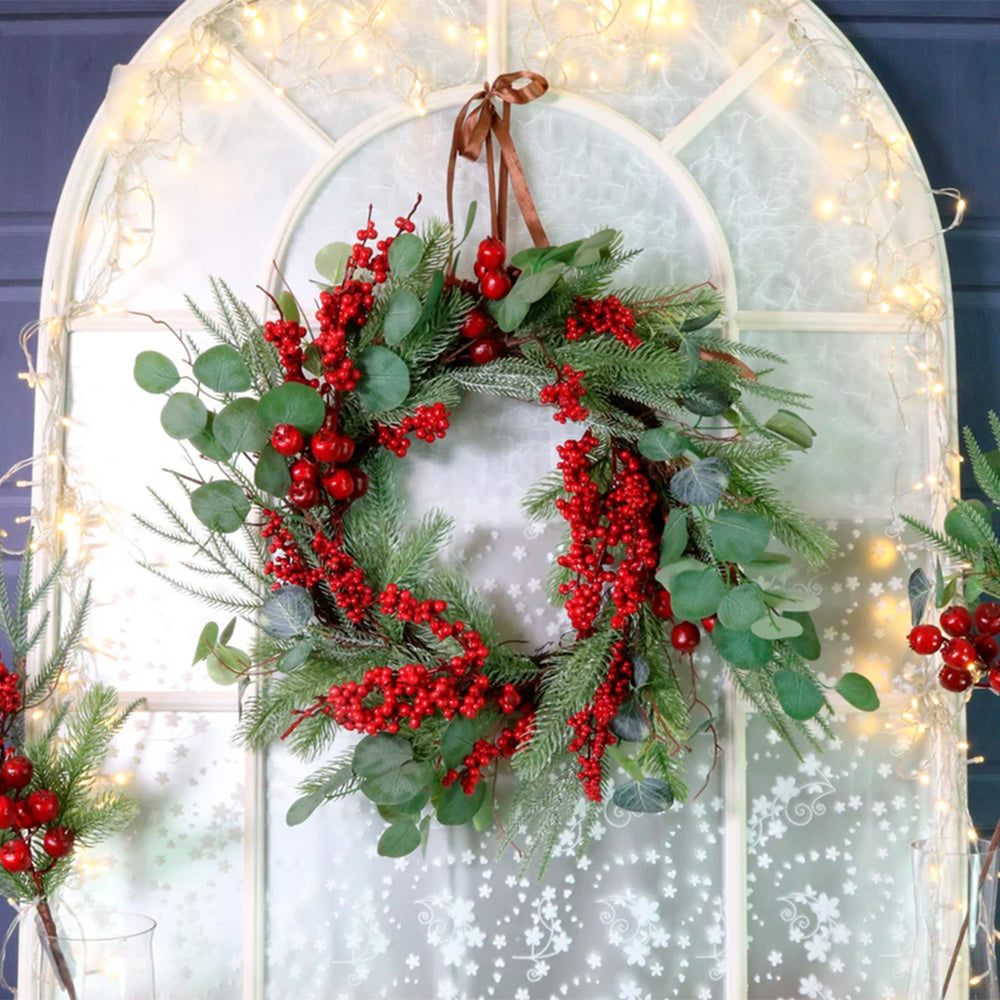 Christmas wreath with red berries and greenery on a decorative archway with fairy lights.