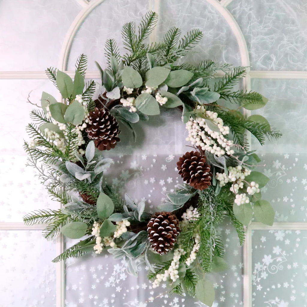 Christmas wreath with greenery, pinecones, and white berries on a decorative glass door.