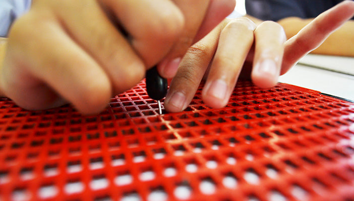 Someone using a red braille frame to produce braille