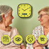 A yellow wall clock with a black frame hangs on a light green wall, shown between two elderly women. The clock has a digital date display and black hands.