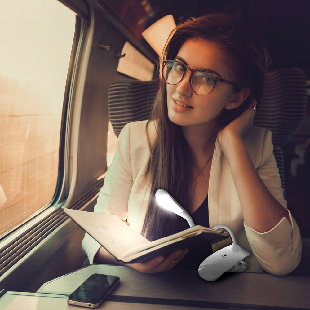 Young woman with spectacles and long brown hair reading a notebook on a train with the clip-on light