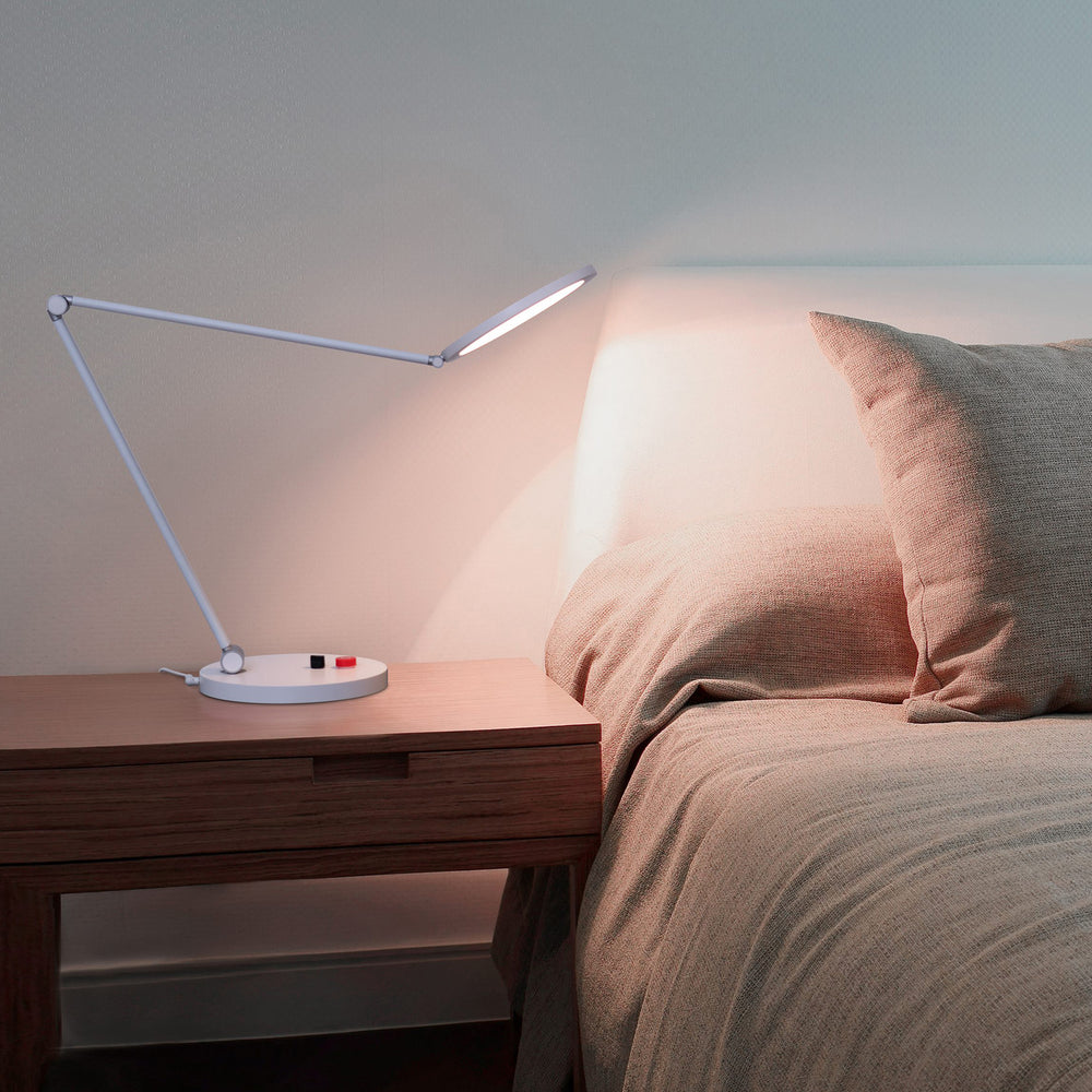 Daylight Tricolour lamp on a bedside table shining light towards the bed
