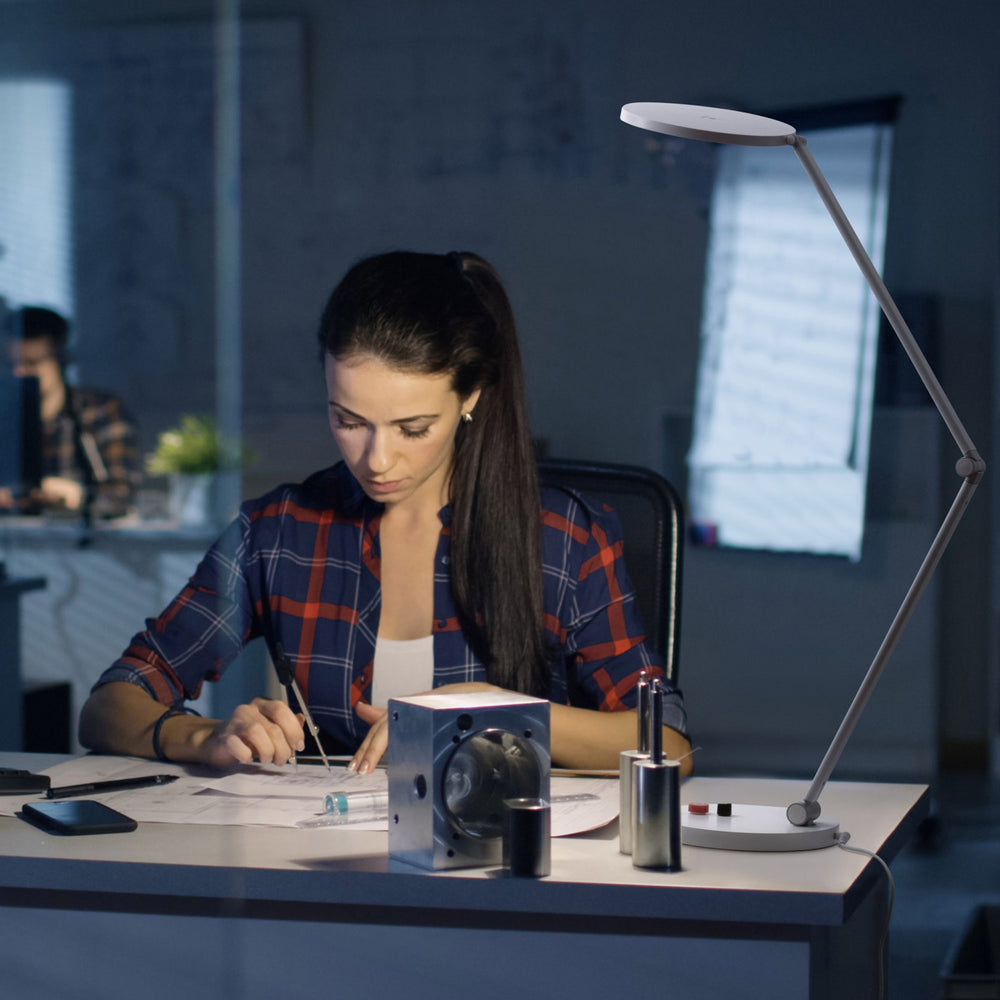 A young white woman working a desk using the Tricolour lamp to illuminate her work