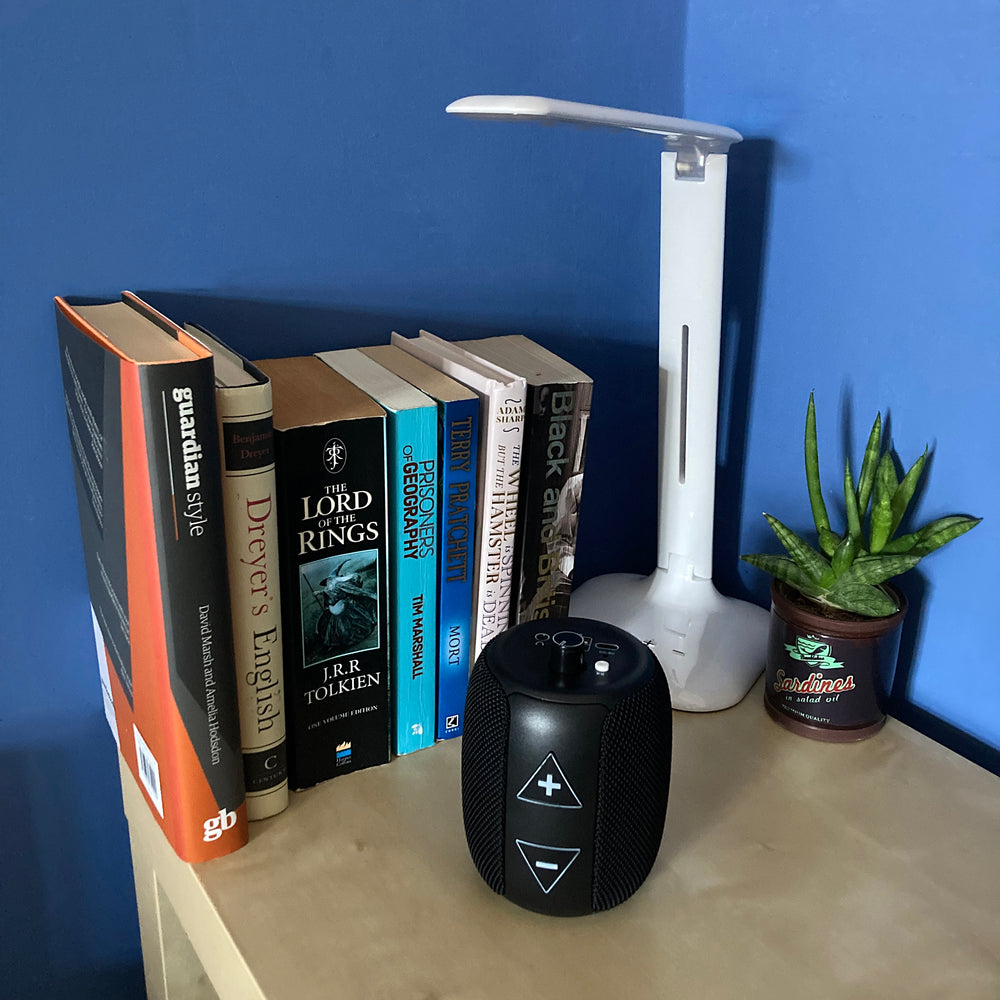 RNIB Accord on a bedside table in front of some books, a light and a small plant