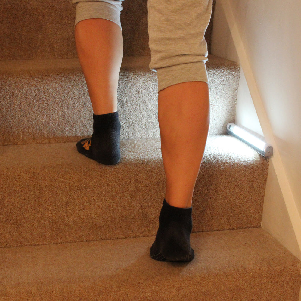 Person wearing black socks on a carpeted staircase with the sensor light illuminating the step.