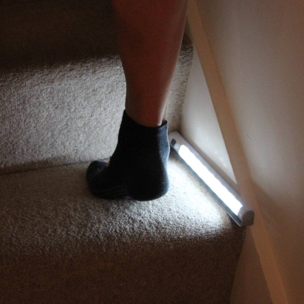 Close up of a person wearing black socks on a carpeted stair with the sensor light illuminating the step.