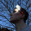 Side view of a person wearing the head torch in the dusk under a winterbare tree. The focus beam is lit and the small red power light is also lit