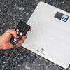Hand holding the IKONN control device next to the IKONN digital scale on a textured surface