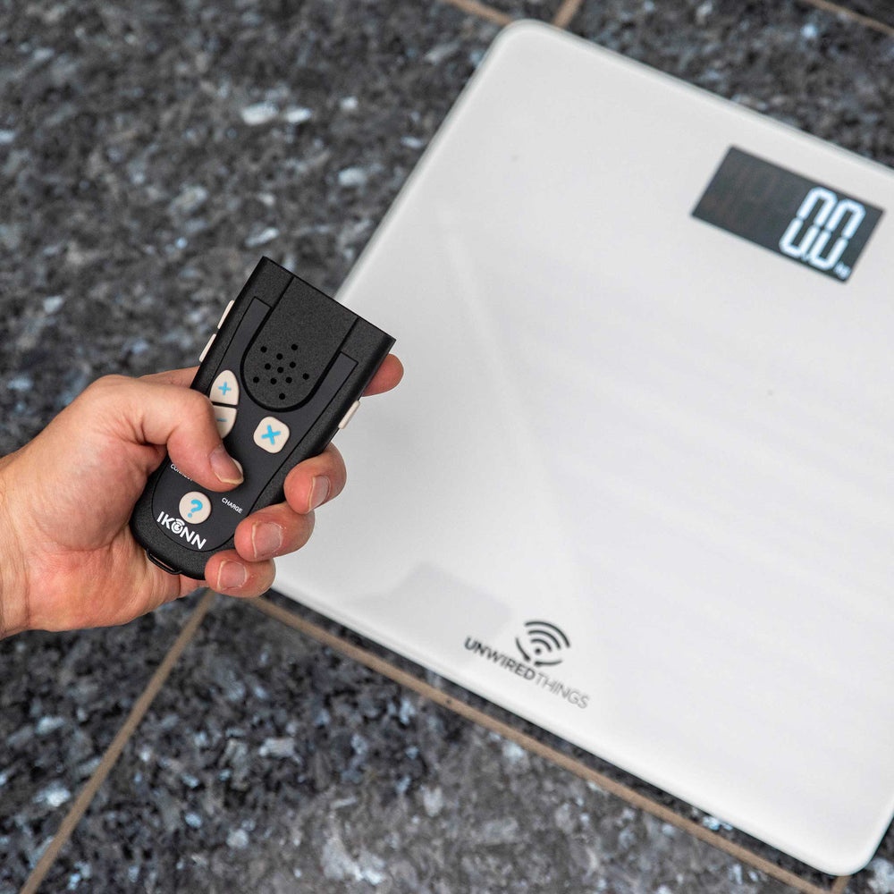 Hand holding the IKONN control device next to the IKONN digital scale on a textured surface