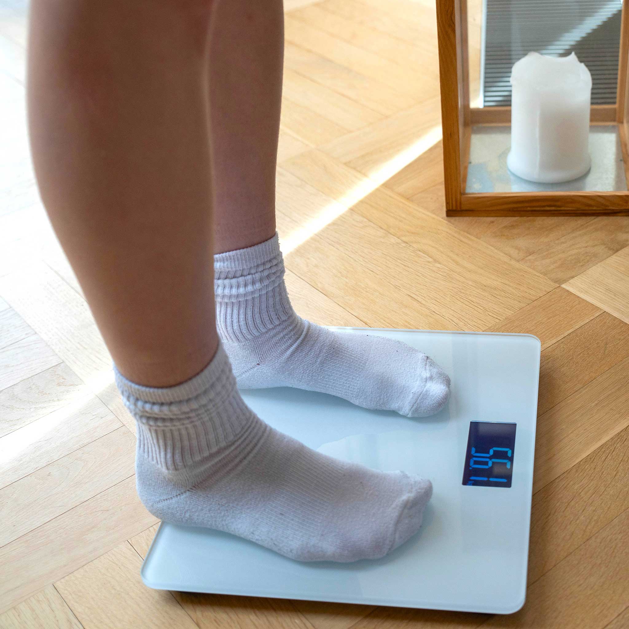 Person standing on a IKONN scale with white socks on a wooden floor.