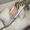 A modern LED lamp with a long white rectangular light bar and a flexible grey neck, shown with a beige sofa with decorative pillows in the background.