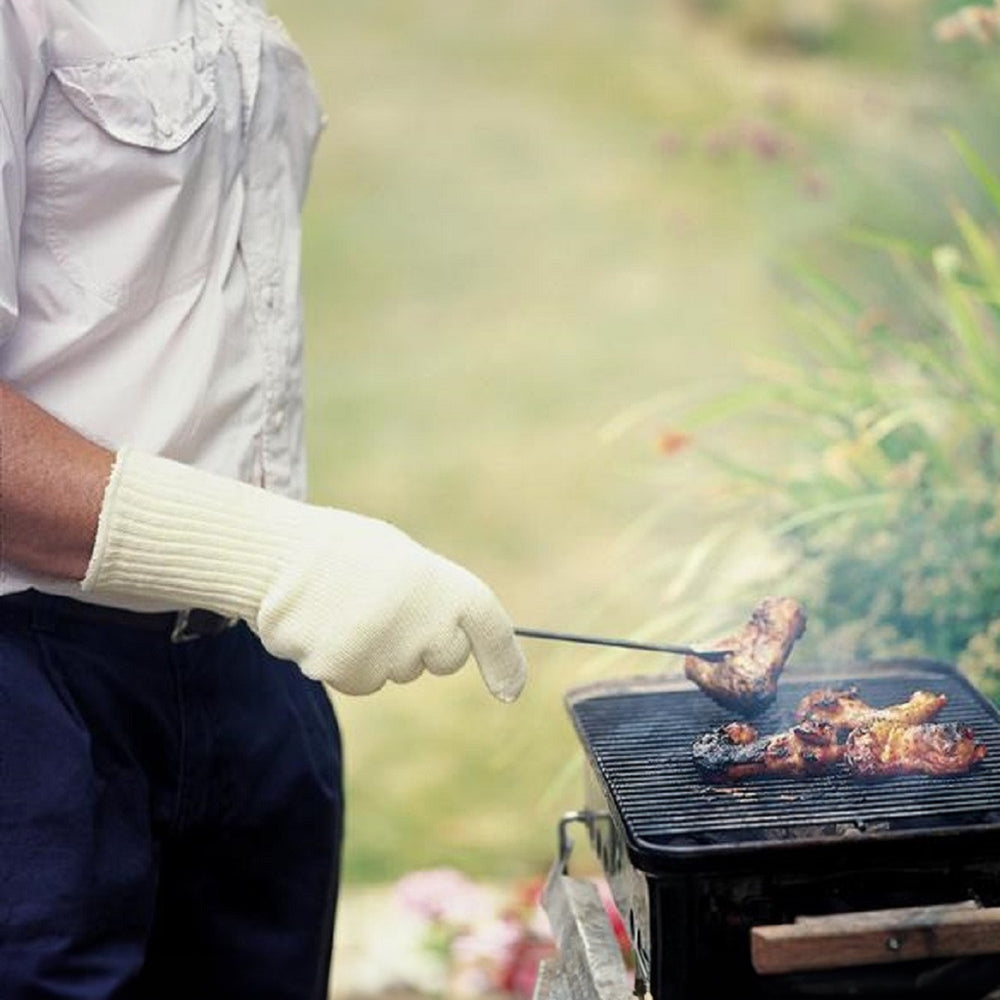 A person wearing the gauntlets to turn meat on a barbecue