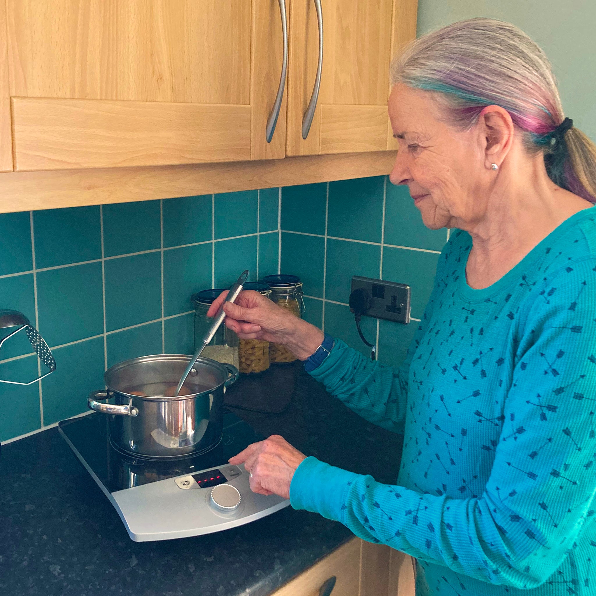An older woman in a turquoise top uses the RNIB Talking induction hob to boil eggs