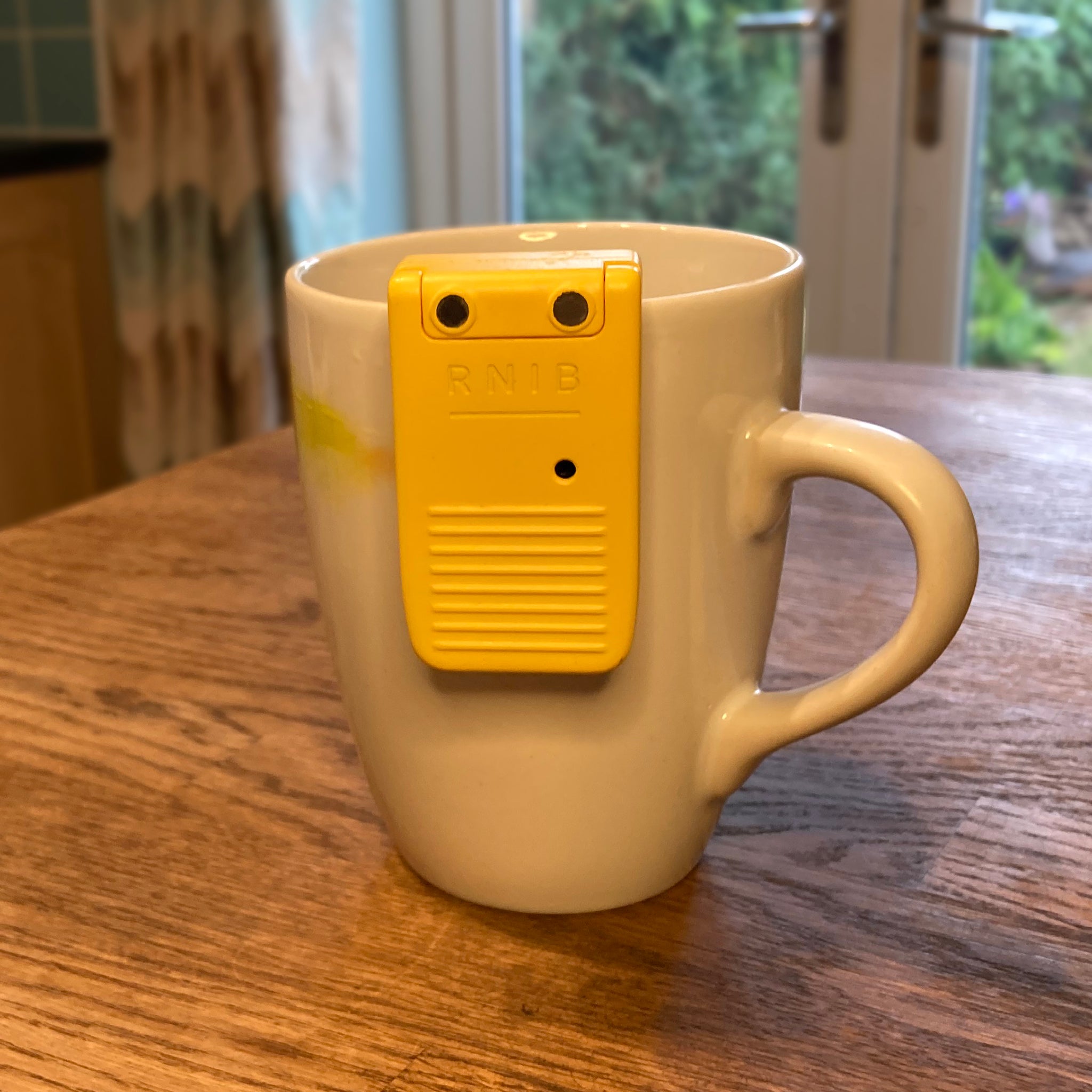 A white and yellow mug on a wooden table top. The liquid level indicator is positioned on the cup ready for measuring liquid.