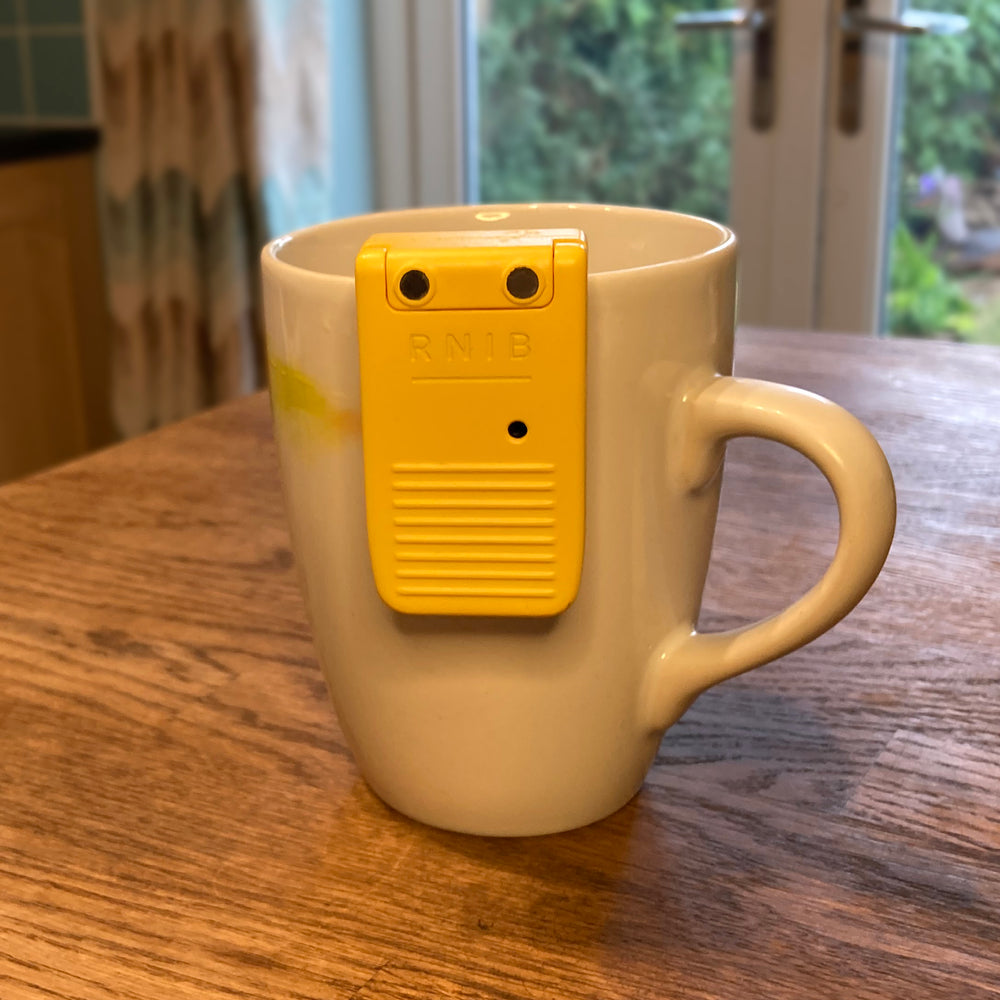 A white and yellow mug on a wooden table top. The liquid level indicator is positioned on the cup ready for measuring liquid.