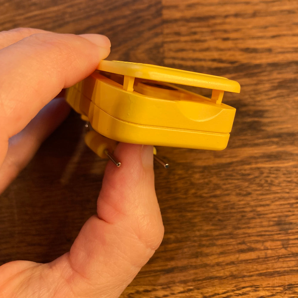 Hand holding RNIB liquid level indicator with the battery compartment slightly open.