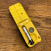 Liquid level indicator with battery compartment open with a AAA battery inside, this is on a wooden surface.