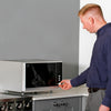 The RNIB talking microwave on a counter top in a kitchen setting A man wearing a dark blue shirt and grey trousers is using the controls to set the timer.