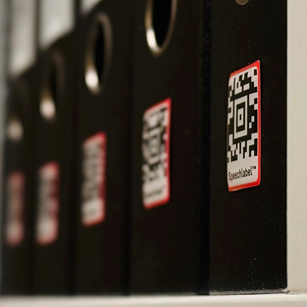 Black binders with red labels and QR codes on a shelf.