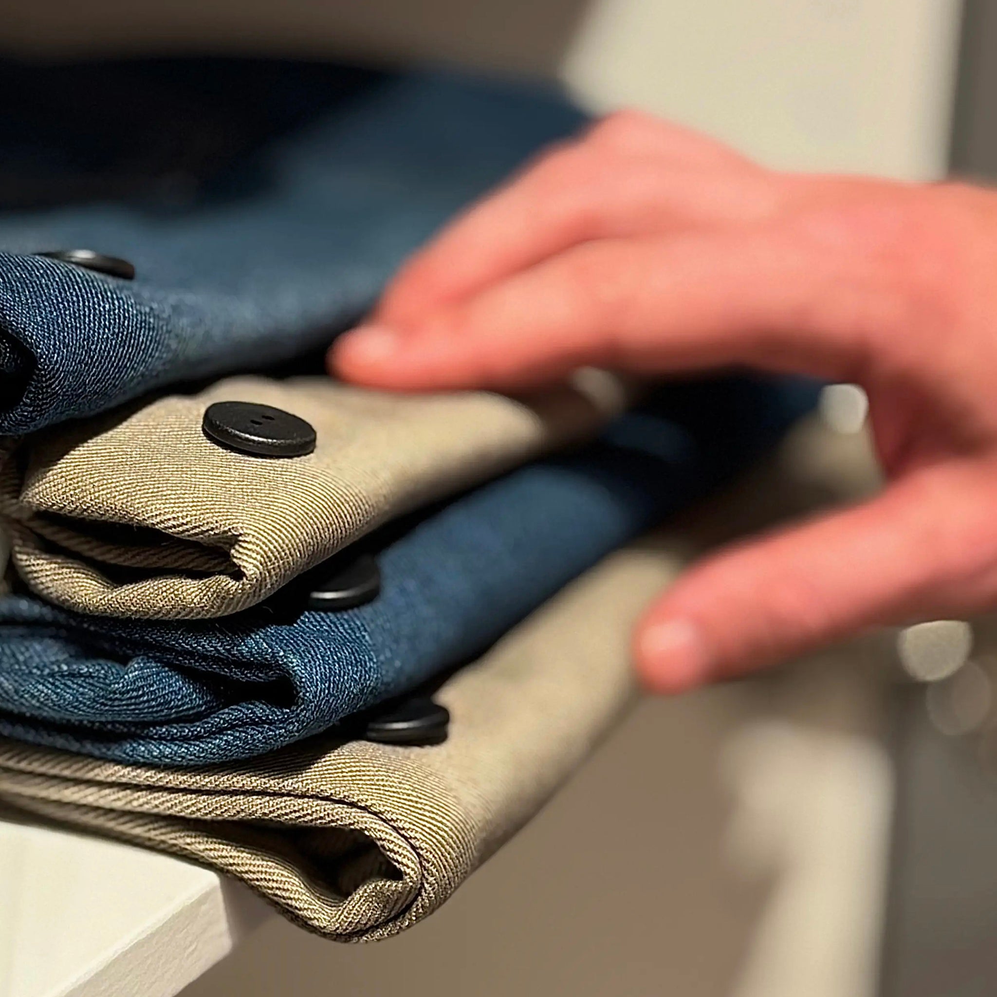 Folded jeans with laundry label buttons being adjusted by a hand on a white surface.