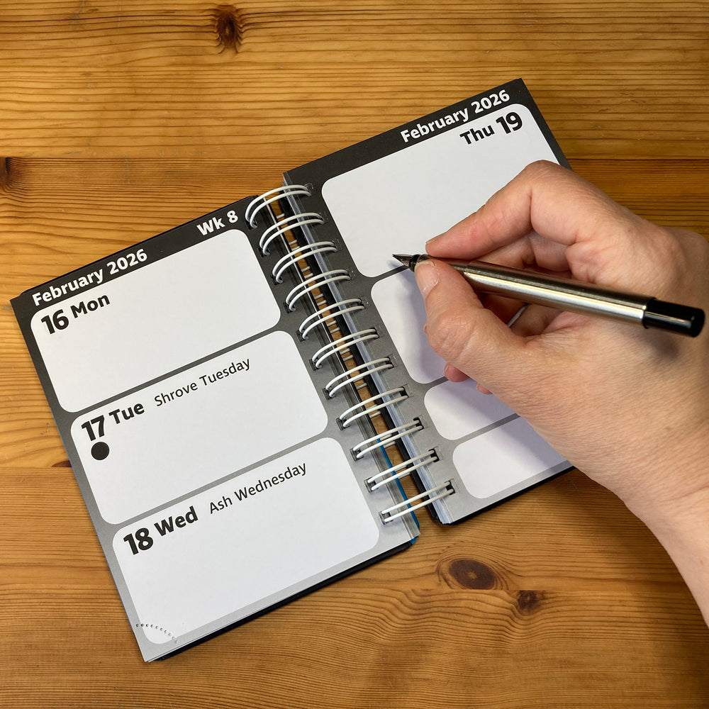 Hand writing in a spiral-bound calendar on a wooden surface