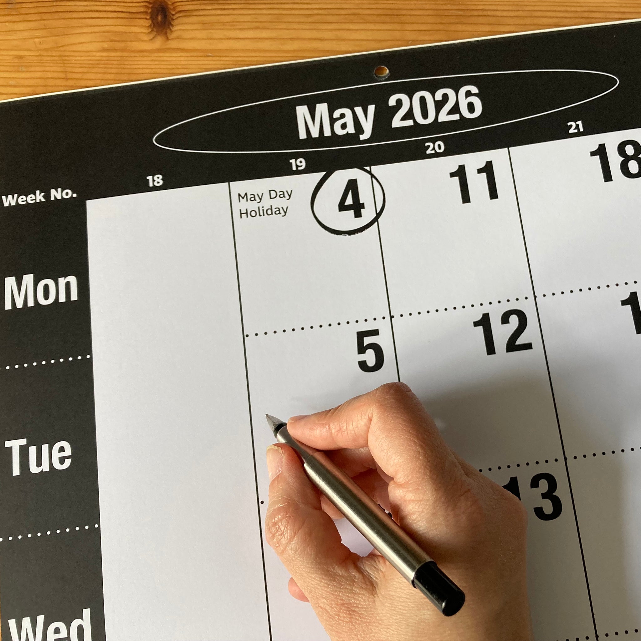 Hand writing on a May 2026 calendar with a pen.