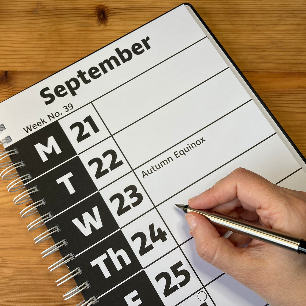 Calendar page for September with a hand holding a pen on a wooden surface