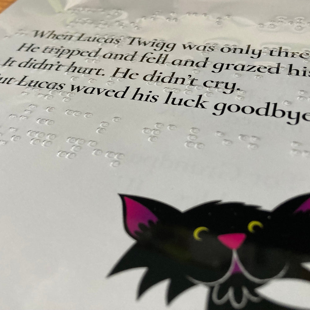 Open book with a black cat illustration on the page with text and braille.