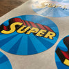 Circular stickers with superhero-themed design with braille.