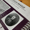 Book page with a portrait and text about Louis Braille on a wooden surface.
