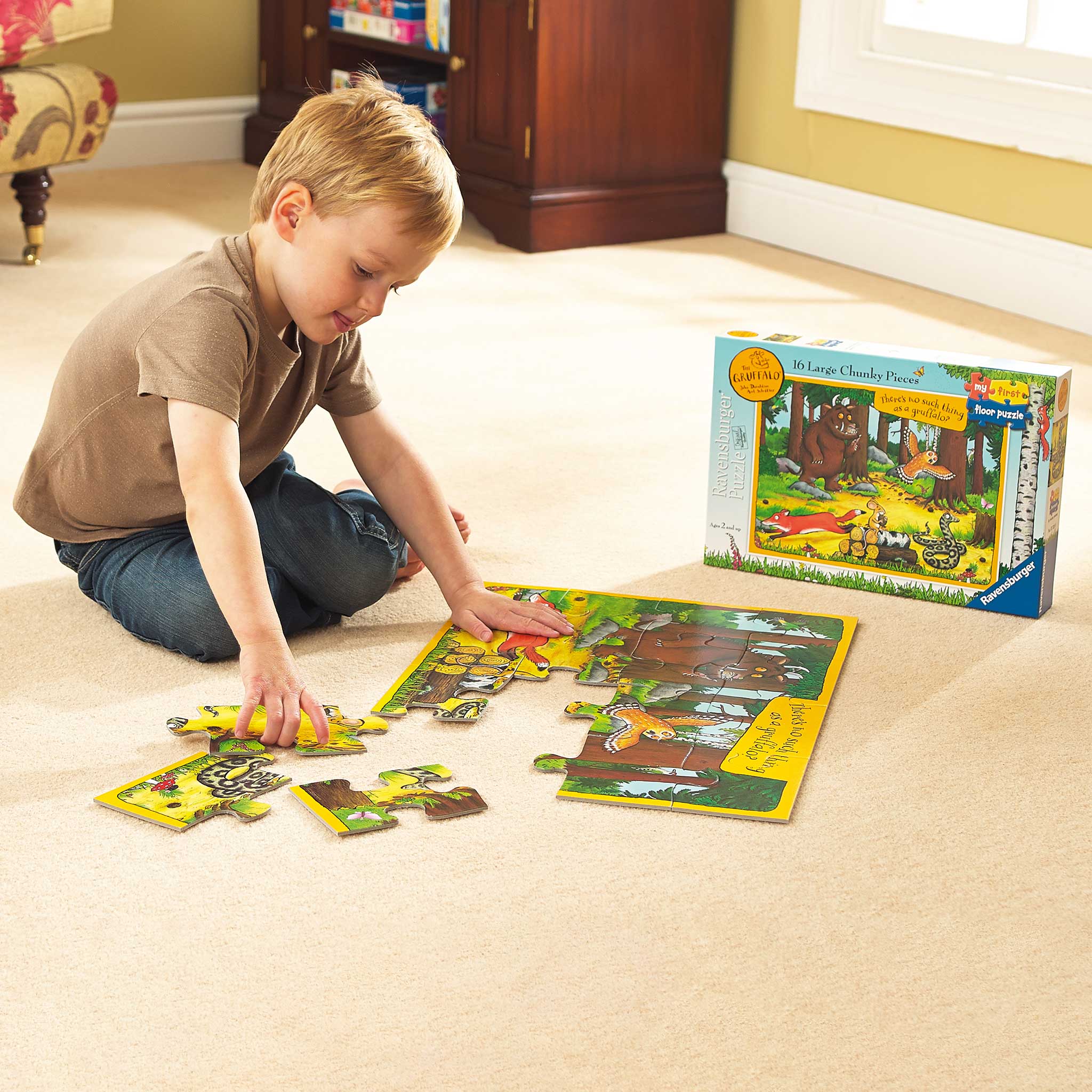 A young child completes the Gruffalo jigsaw on a beige carpet