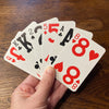 A hand holding large print playing cards fanned out with a wooden table behind them.