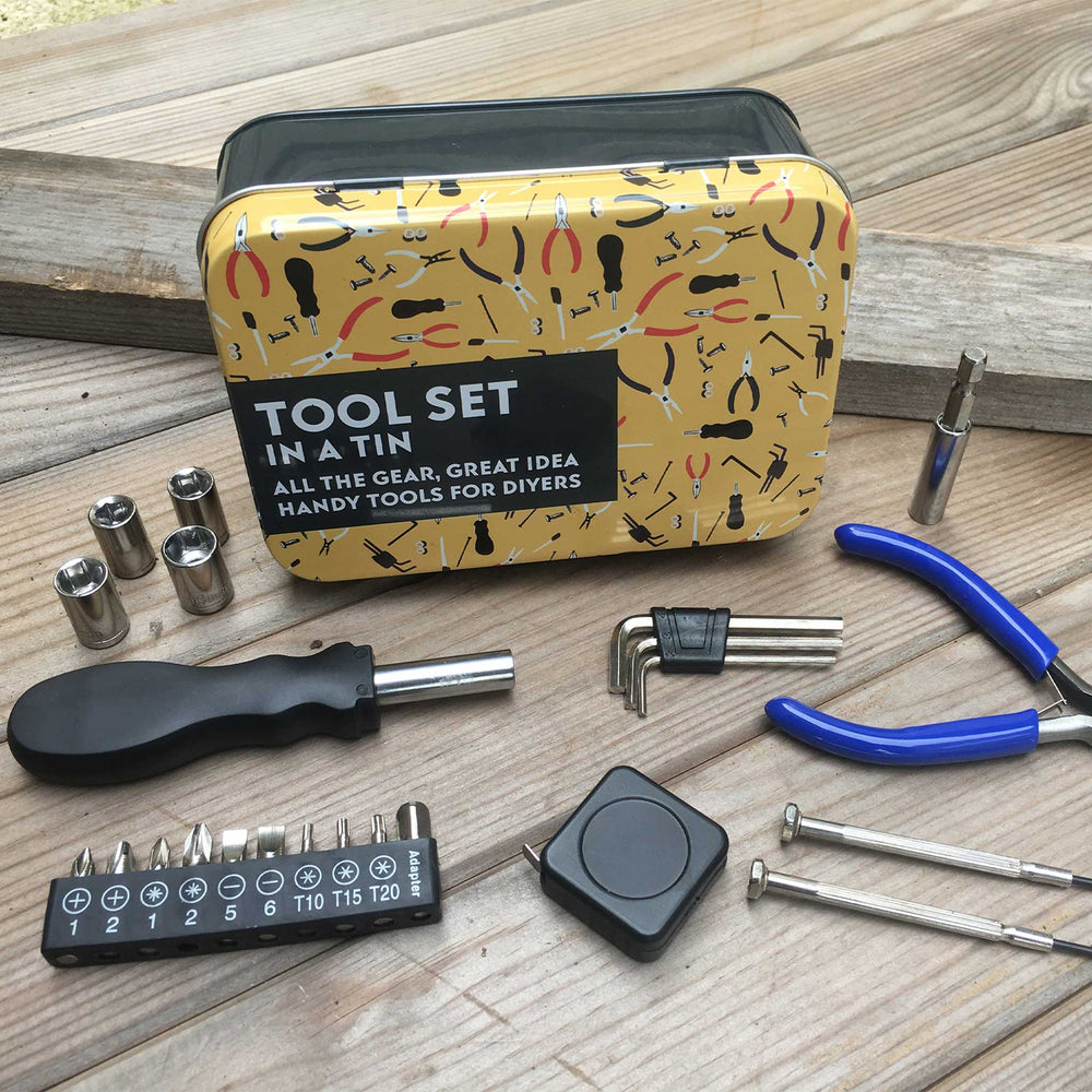 A 10-piece hand tool set displayed on a wooden surface next to its decorative tin case. The set includes various metal tools such as sockets, hex keys, screwdrivers, and blue-handled pliers, alongside a black-handled tool with a silver metal head.