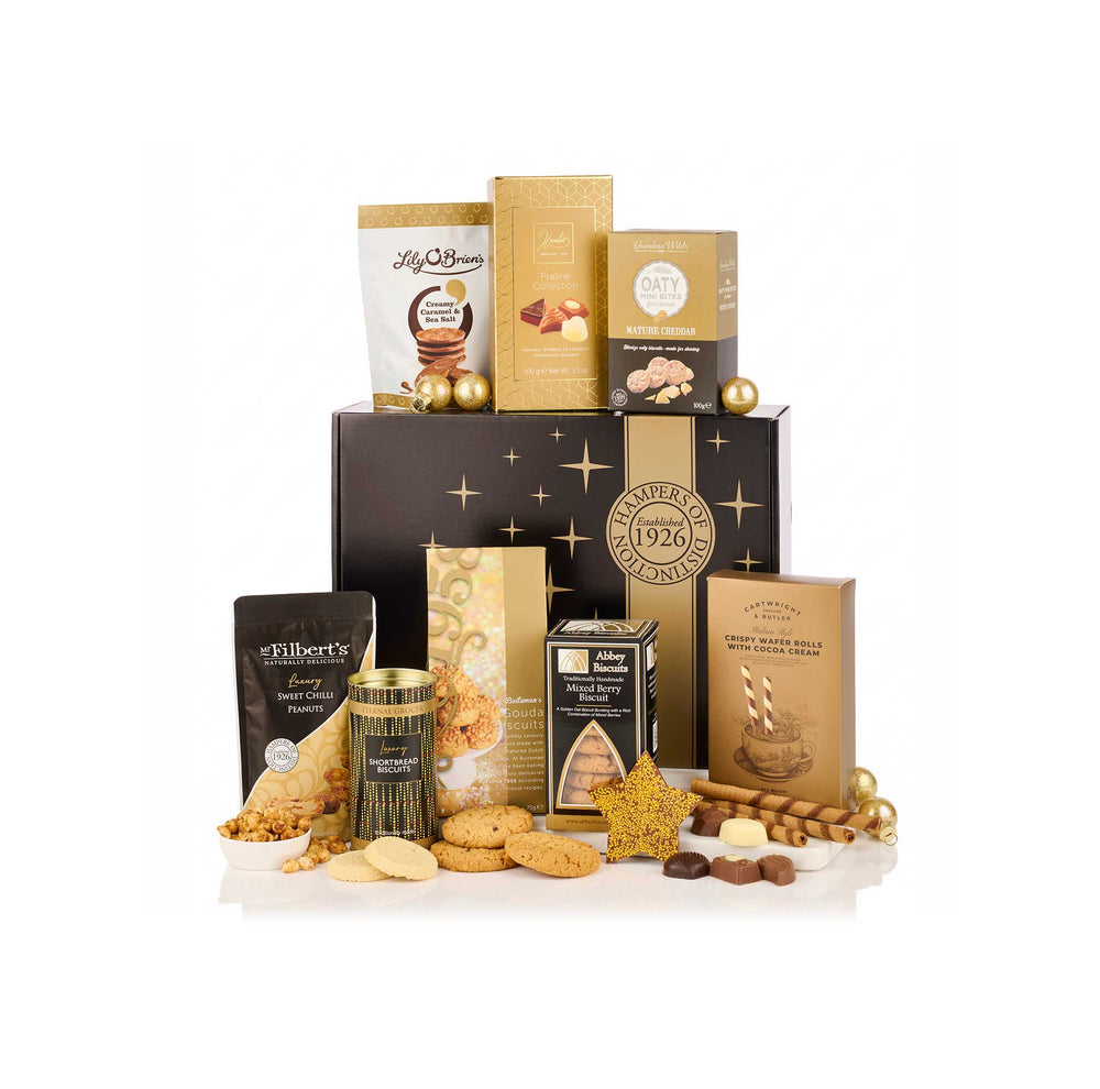 A luxury gourmet food gift hamper featuring an assortment of chocolates, biscuits, and treats arranged in front of a black and gold gift box on a white background. Visible brands include Lindt, Lindt Belgium, and Lindt's.